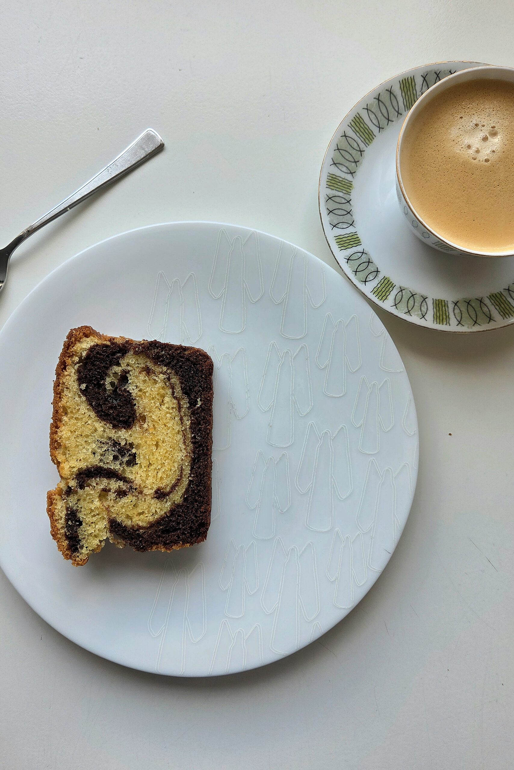 Slice of Norwegian marble cake on a white plate with a cup of coffee
