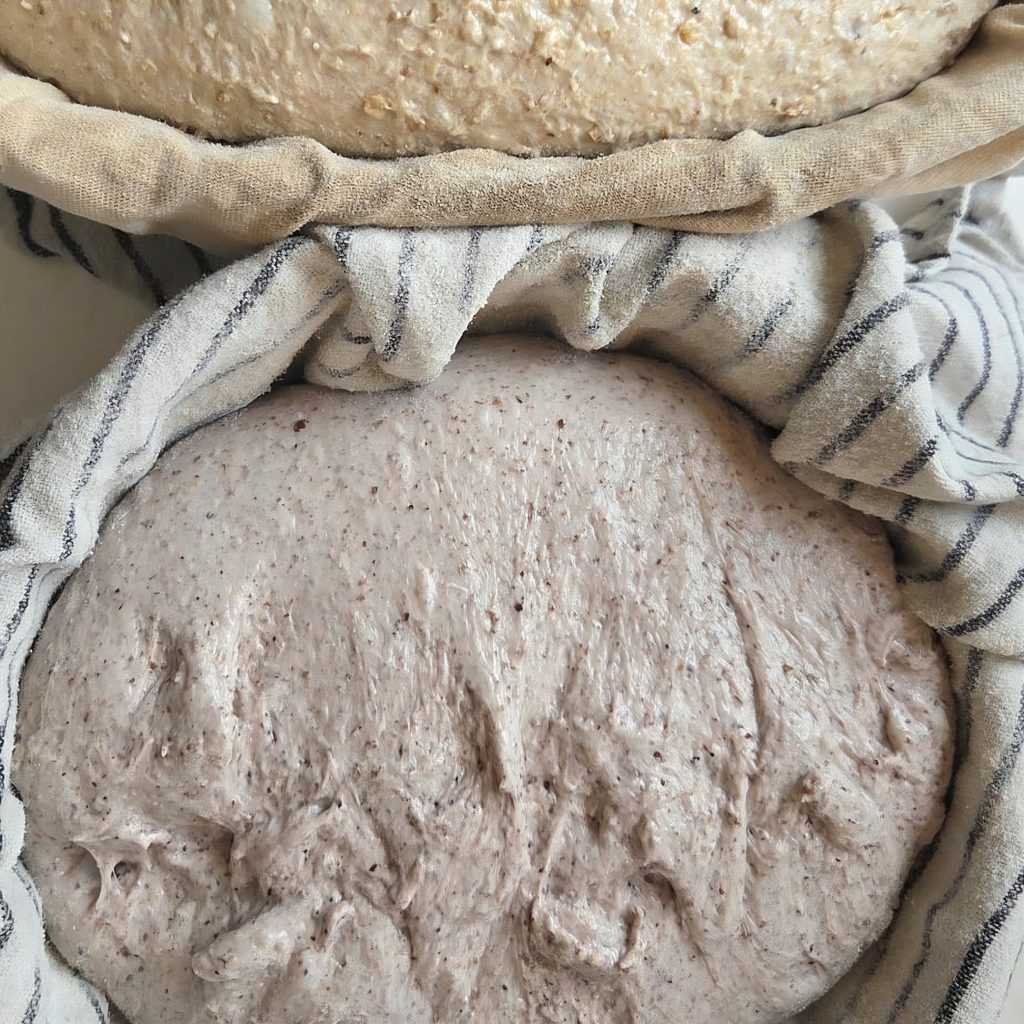 Shaped sourdough loaf resting seam-side up in a linen-lined banneton, dusted with rice flour