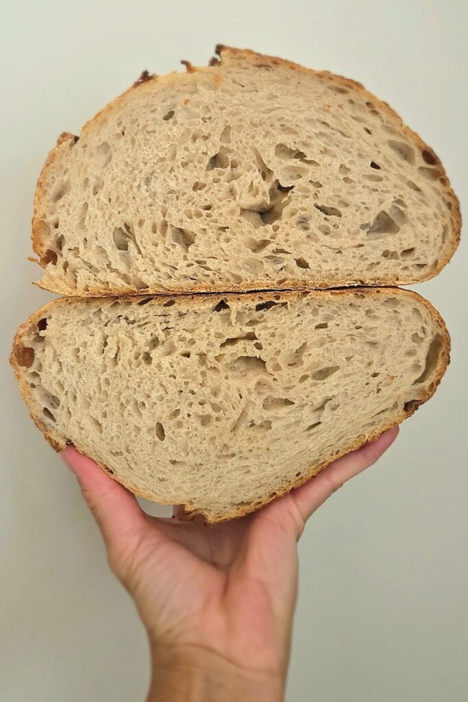 Sliced sourdough loaf with a crackly golden crust and open crumb, baked with steam at high heat
