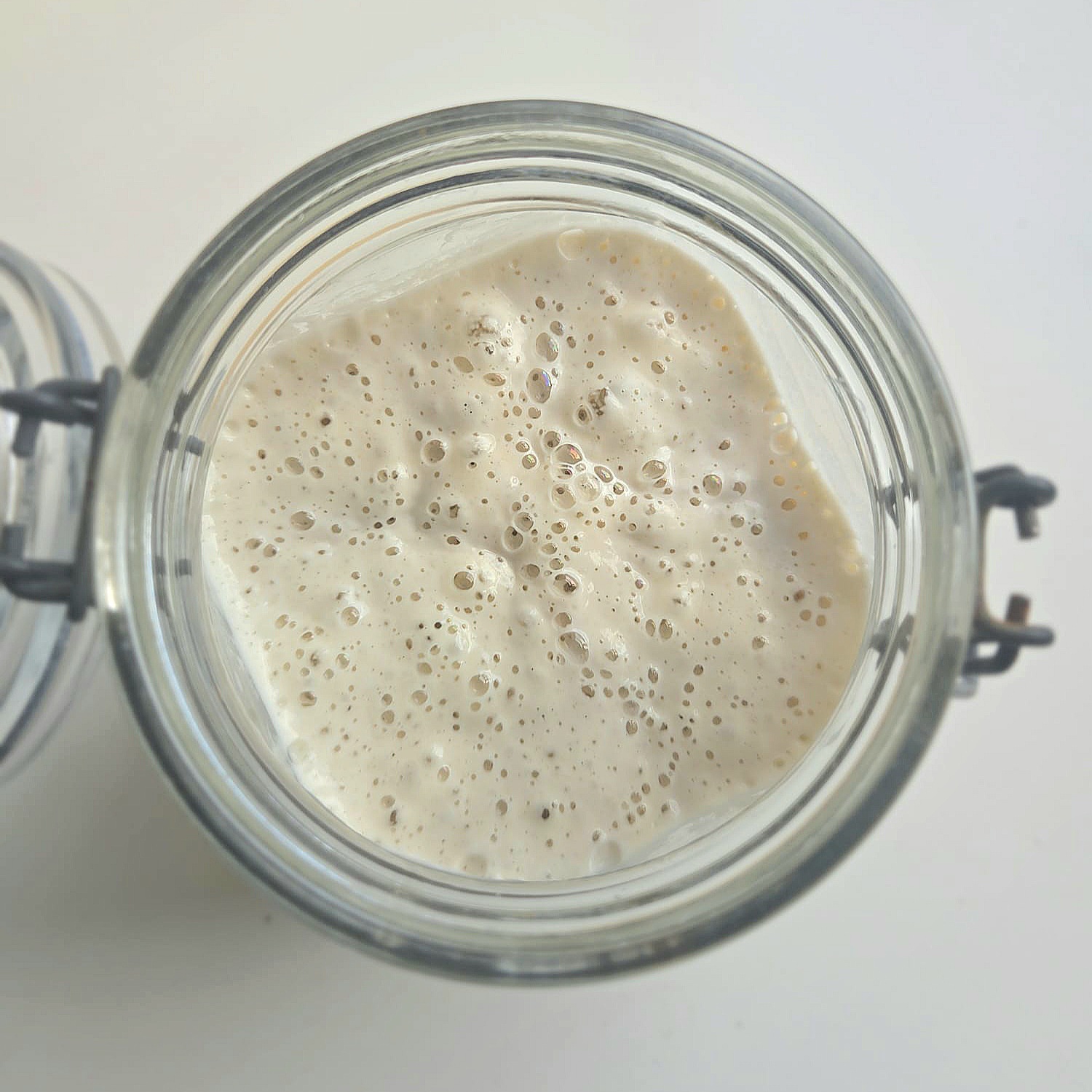 Active sourdough starter full of bubbles, seen from above in a glass jar