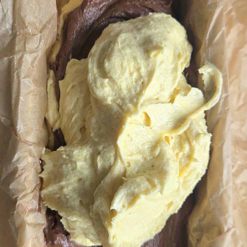 Vanilla batter spooned over cocoa batter in a parchment-lined loaf pan