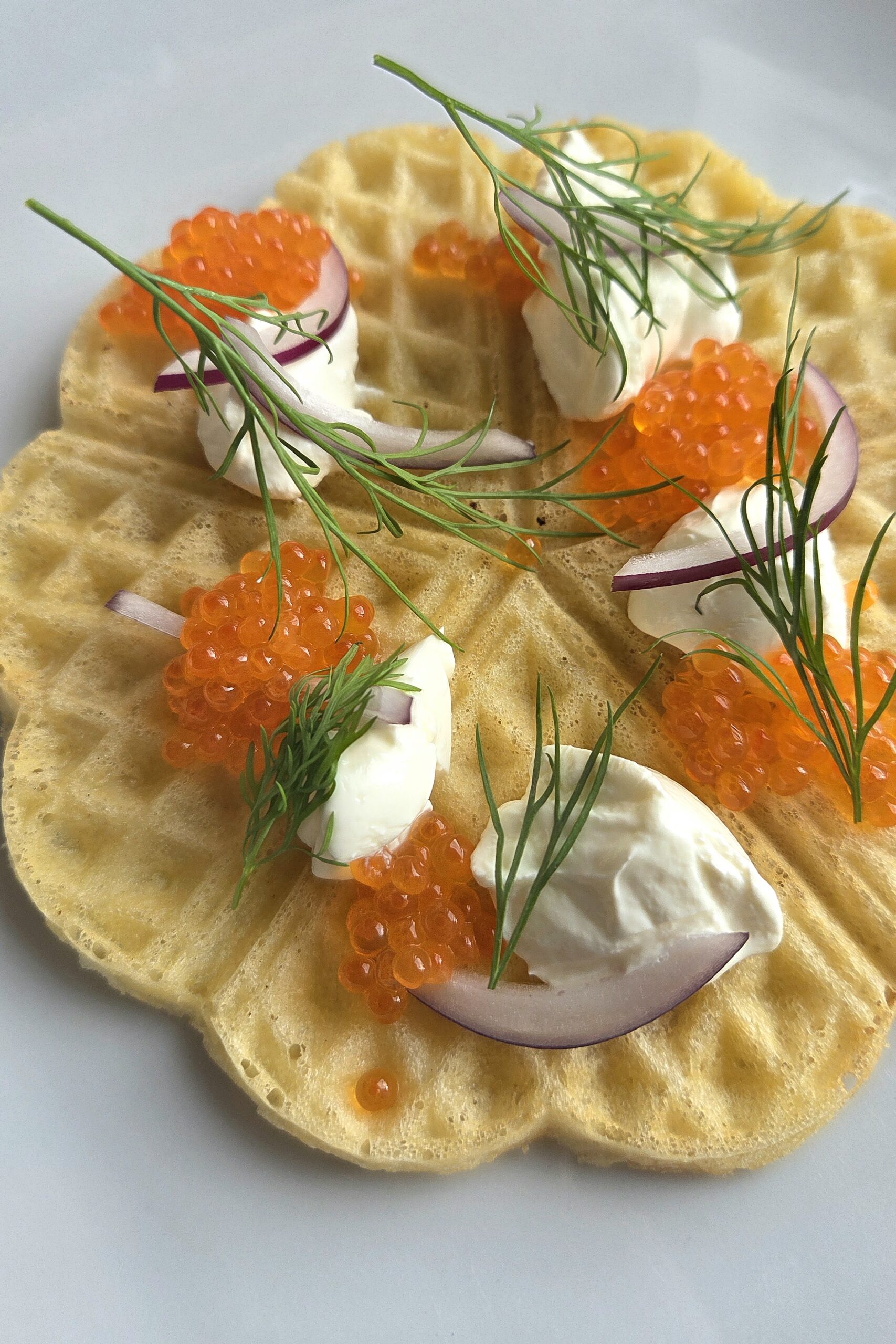 Angled view of a waffle with sour cream, salmon roe, red onion and fresh dill