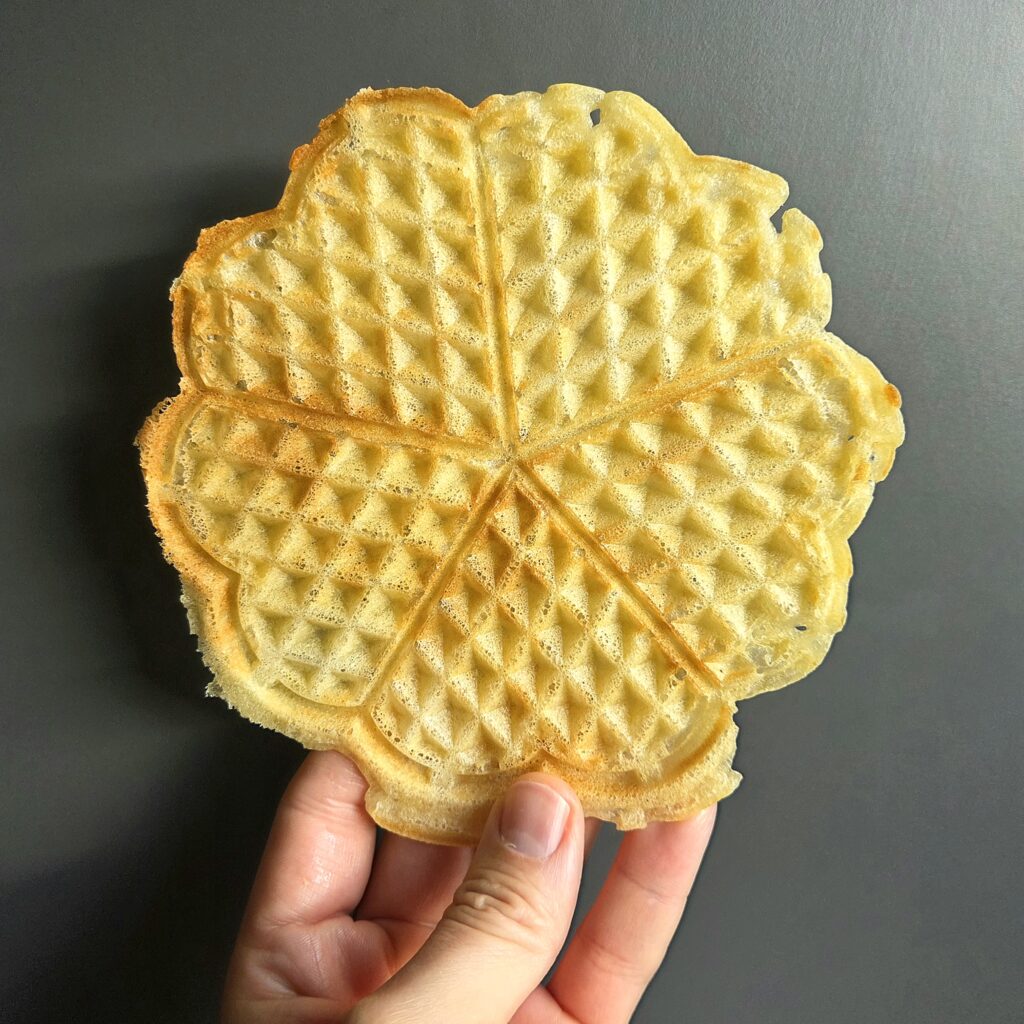Hand holding a thin, golden, crunchy heart-shaped waffle