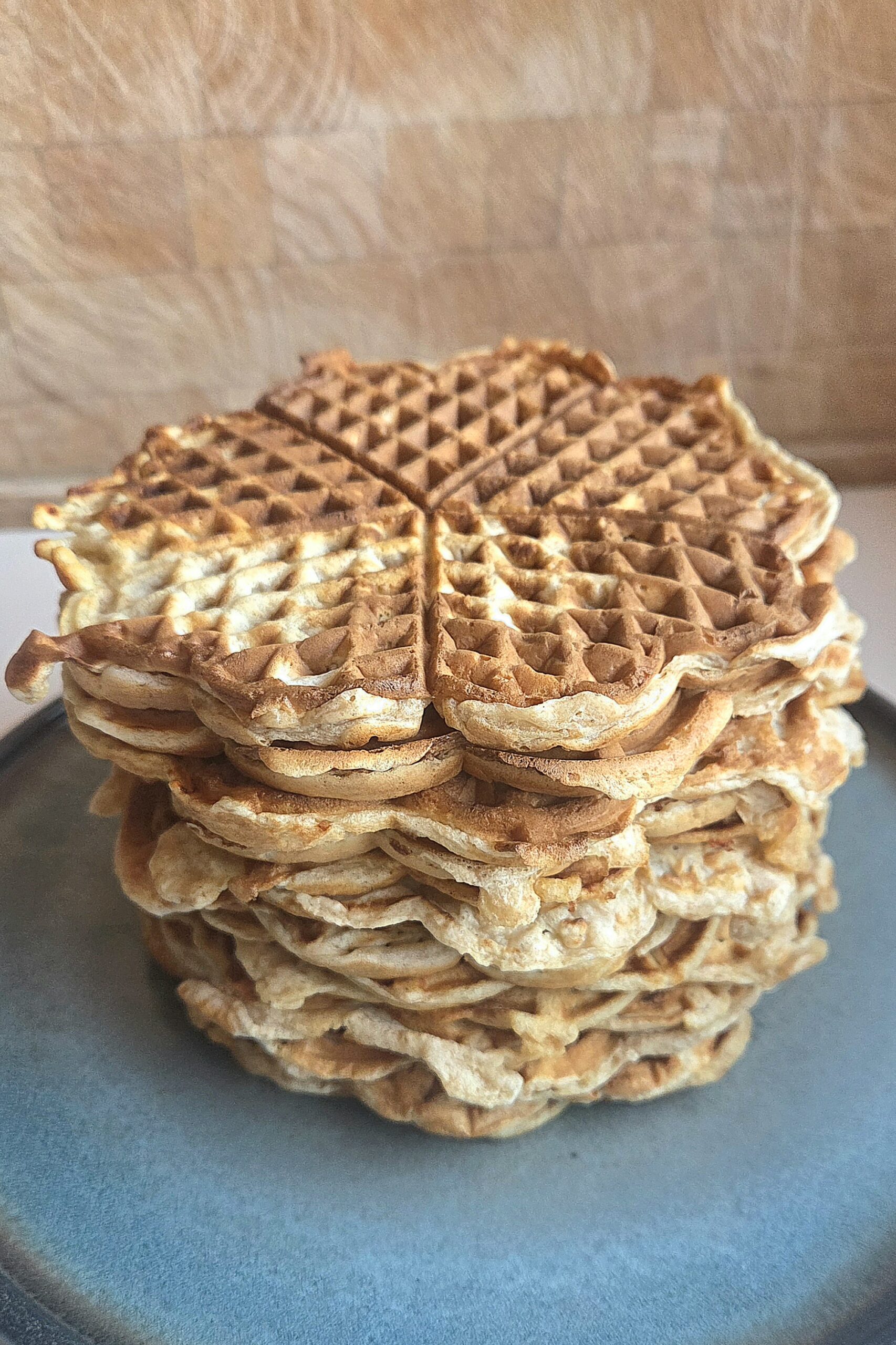 Whole wheat waffles stacked on a gray stoneware plate, the top heart waffle showing a golden-brown grid