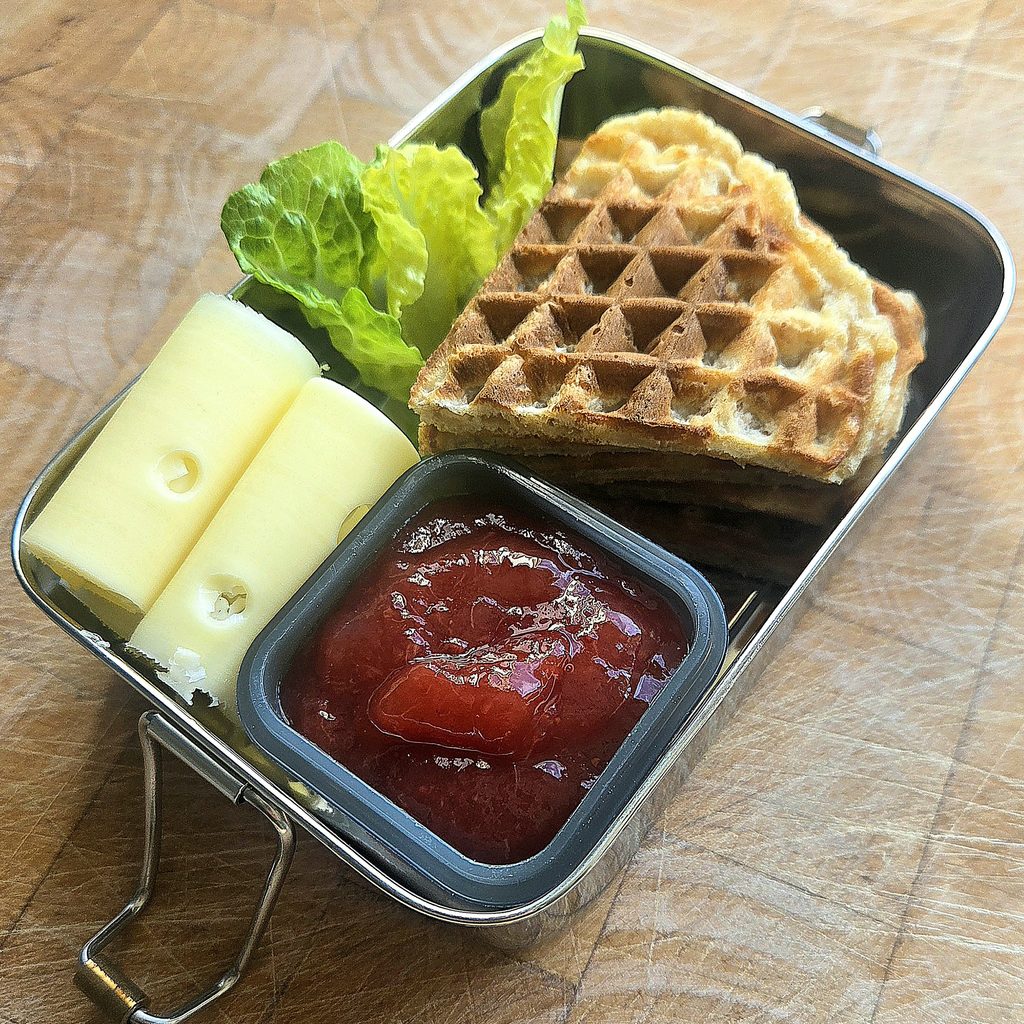 Whole wheat waffle with butter, romaine and rolled cheese slices seen from above