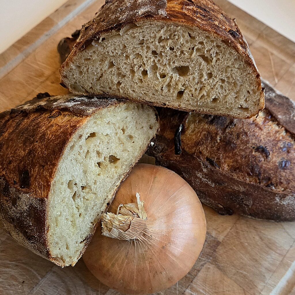 Two halves of French onion soup sourdough showing the crumb and onion pieces baked dark into the crust