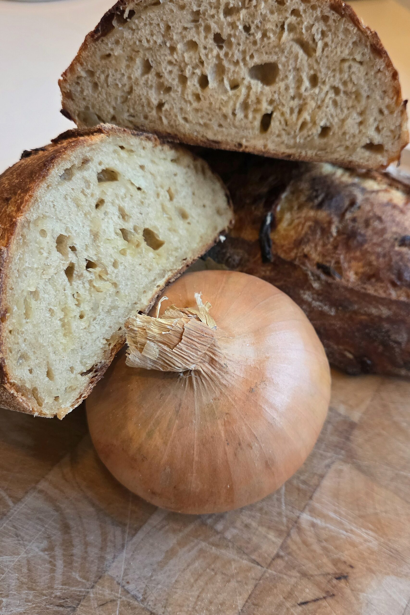 Close view of French onion soup sourdough crumb with a whole yellow onion in front of the cut loaves