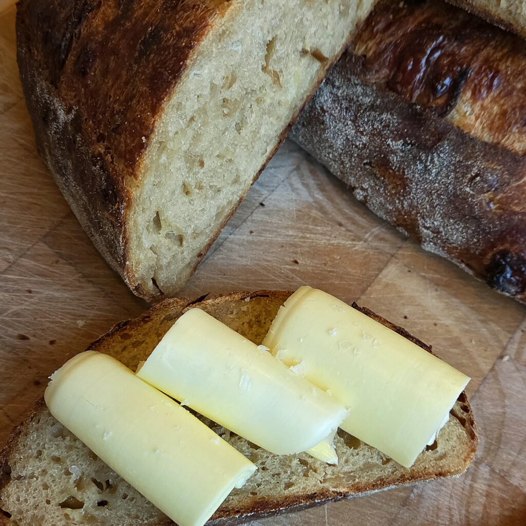 Slice of French onion soup sourdough topped with curls of butter and flaky salt, the cut loaf behind it